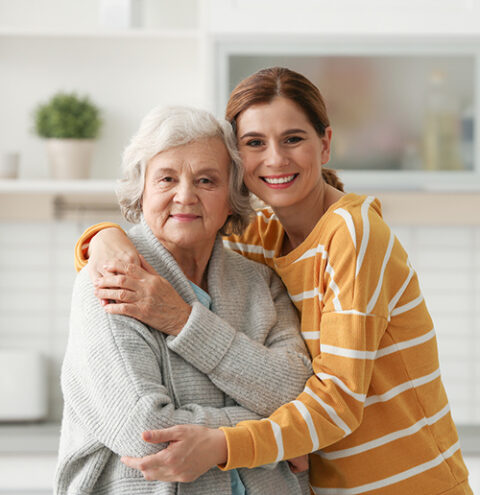 Elderly Woman With Female Caregiver In Kitchen. Space For Text